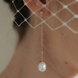 A bride wears gold long crystal & baroque pearl drop earrings