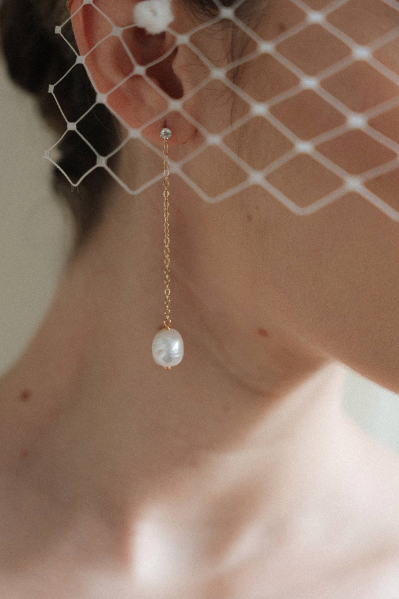 A bride wears gold long crystal & baroque pearl drop earrings