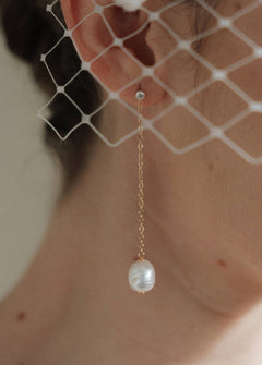 A bride wears gold long crystal & baroque pearl drop earrings