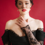 bride wears a gold baroque coin vegan pearl necklace, gold crystal drop earrings and a black tulle mask veil micro veil with a black lace dress