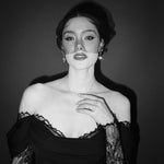 Black and white portrait of a bride wearing a gold baroque coin vegan pearl necklace, gold crystal drop earrings and a black tulle mask veil micro veil with a black lace dress