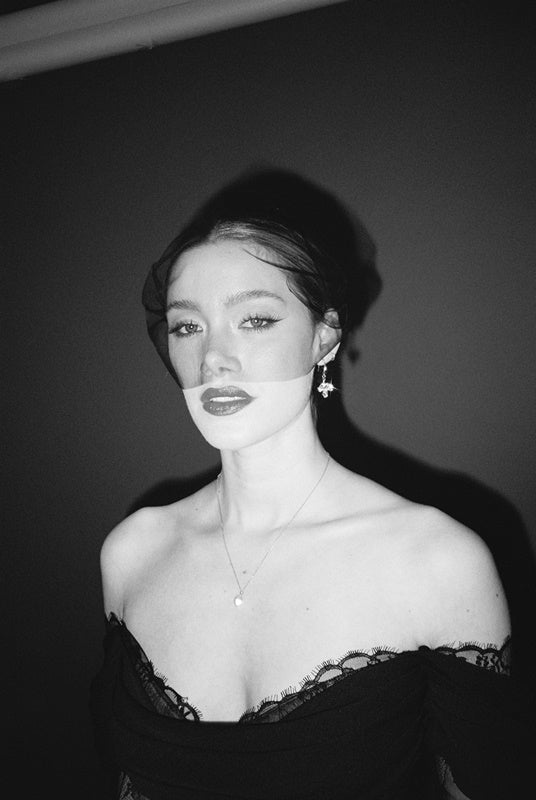 Black and white portrait of a bride wearing a gold baroque coin vegan pearl necklace, gold crystal drop earrings and a black tulle mask veil micro veil with a black lace dress