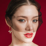 Bride wearing gold crystal drop earrings and a black tulle mask veil against a red background