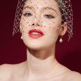 Woman wearing a white strapless dress and crystal birdcage veil against a red background