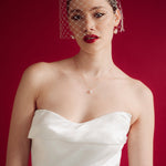 Woman wearing a white strapless dress and crystal birdcage veil against a red background