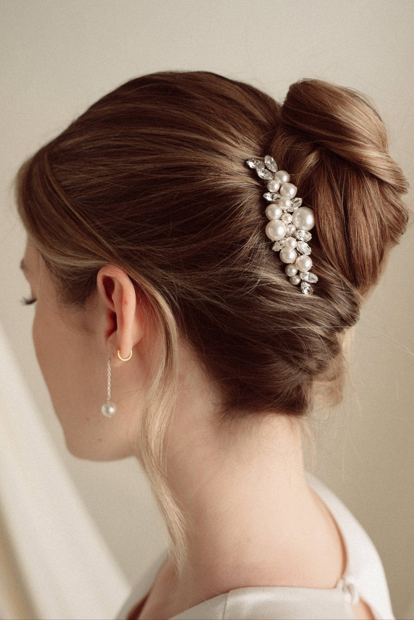 Woman with elegant hair styled in a bun with decorative pearl and crystal comb headpiece against a neutral background