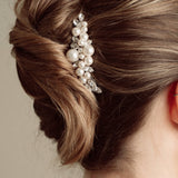 Woman with elegant hair styled in a bun with decorative pearl and crystal comb headpiece against a neutral background