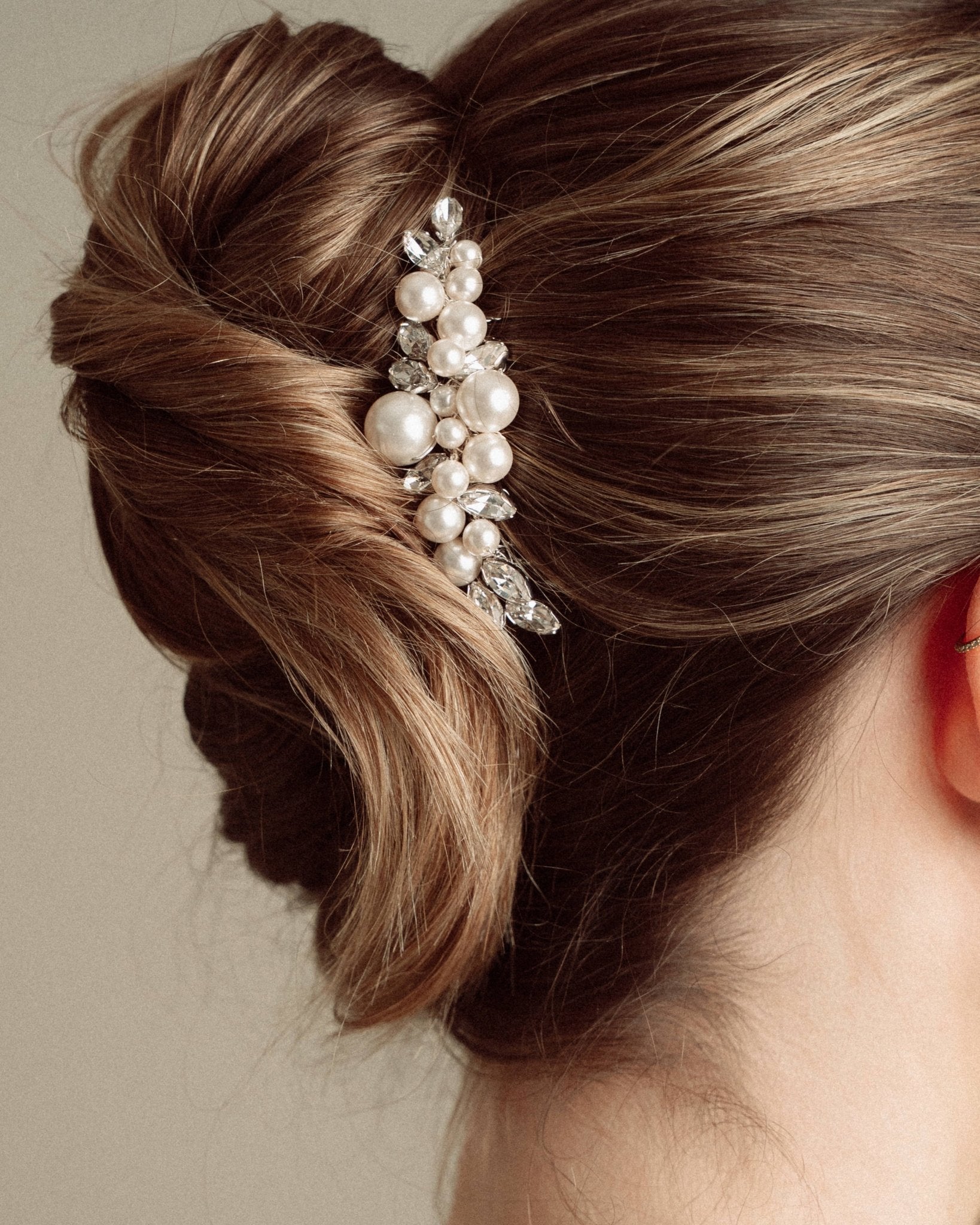 Woman with elegant hair styled in a bun with decorative pearl and crystal comb headpiece against a neutral background
