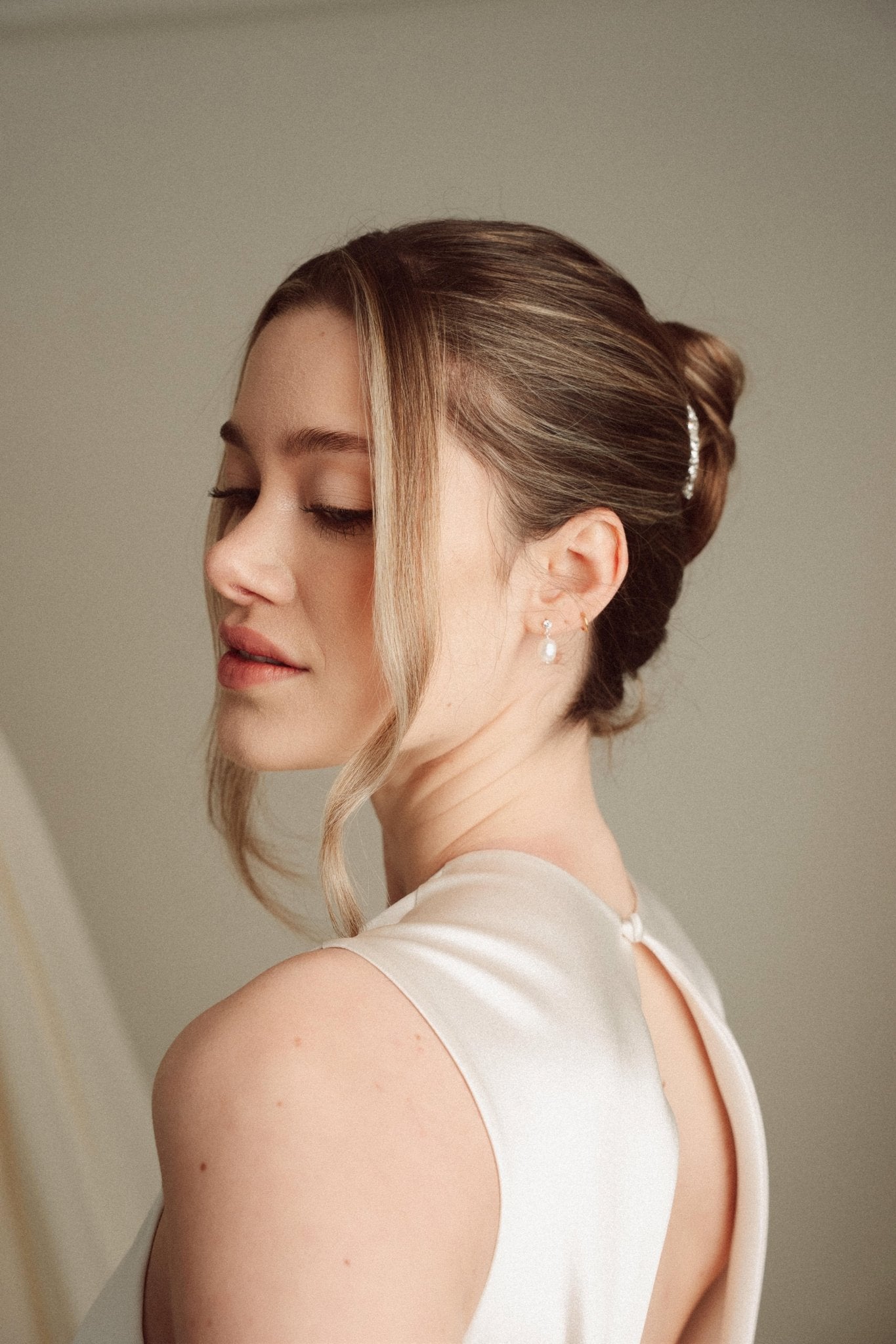 Bride wears pearl and crystal stud drop earrings with a small silver crystal comb with an elegant chignon updo