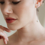 Close-up of a woman wearing silver crystal pearl drop earrings with a neutral background