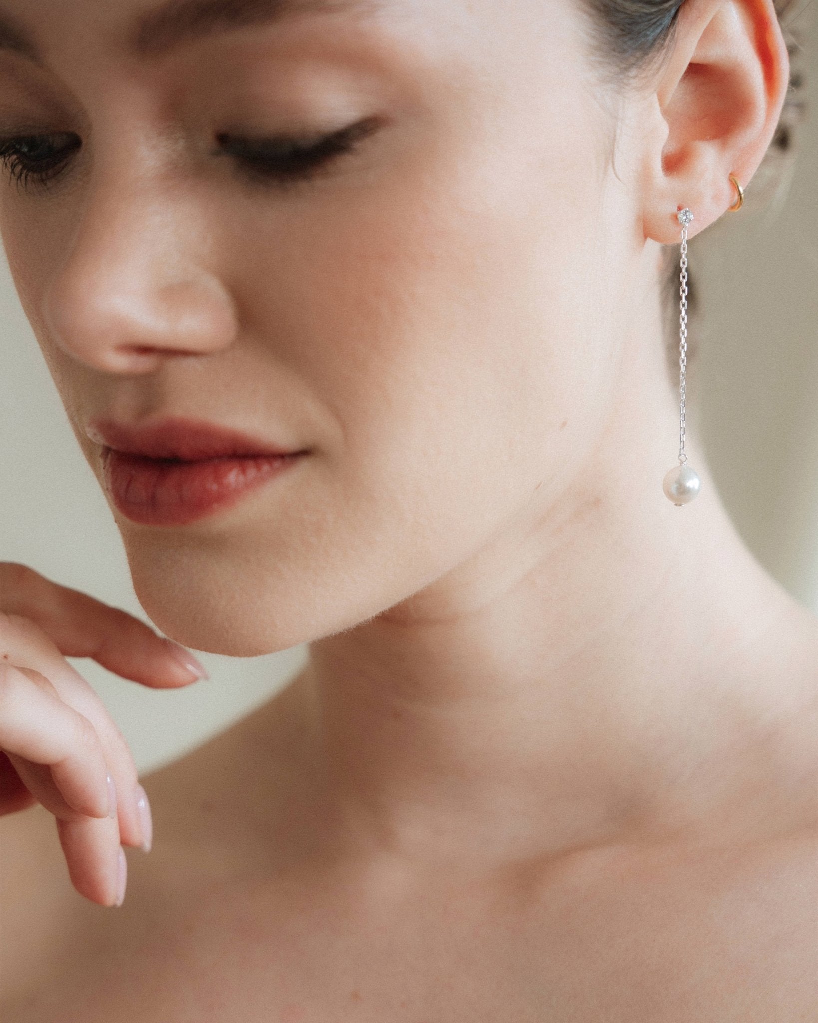 Close-up of a woman wearing silver crystal pearl drop earrings with a neutral background