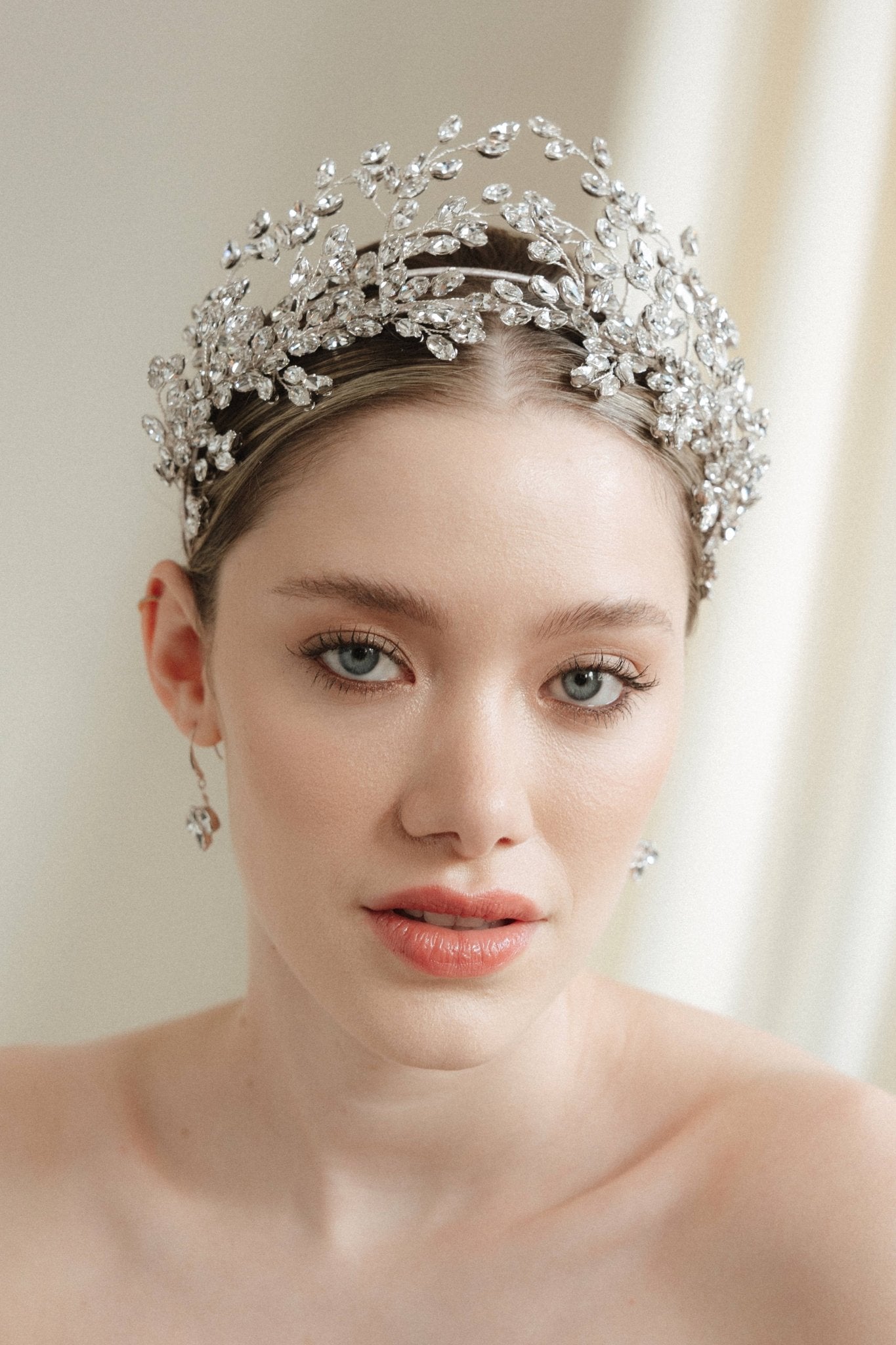 A bride wears a statement silver crown tiara with matching hair pins extending over the head.