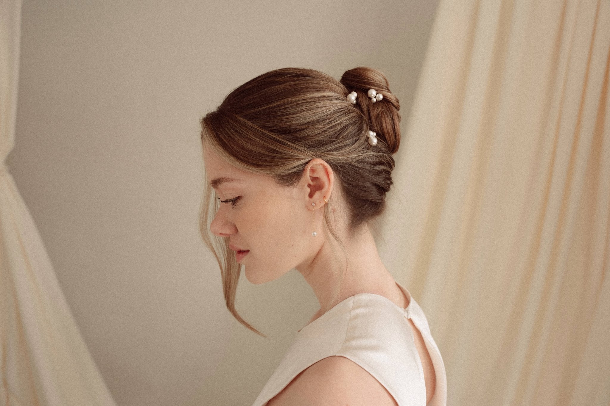 Bride wears pearl cluster hair pins and crystal and perl delicate drop earrings  with a silk gown and soft romantic chignon updo