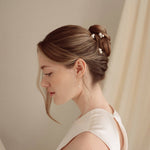 Bride wears pearl cluster hair pins and crystal and perl delicate drop earrings  with a silk gown and soft romantic chignon updo