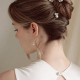 Bride wears pearl cluster hair pins and crystal and perl delicate drop earrings  with a silk gown and soft romantic chignon updo