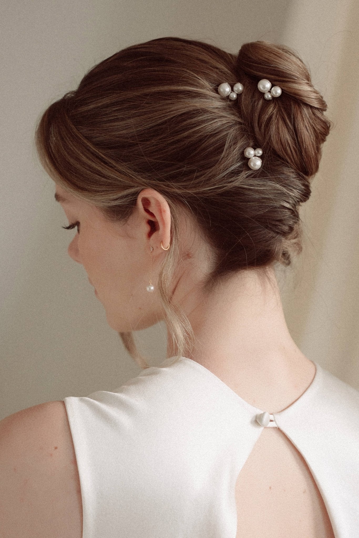 Bride wears pearl cluster hair pins and crystal and perl delicate drop earrings  with a silk gown and soft romantic chignon updo