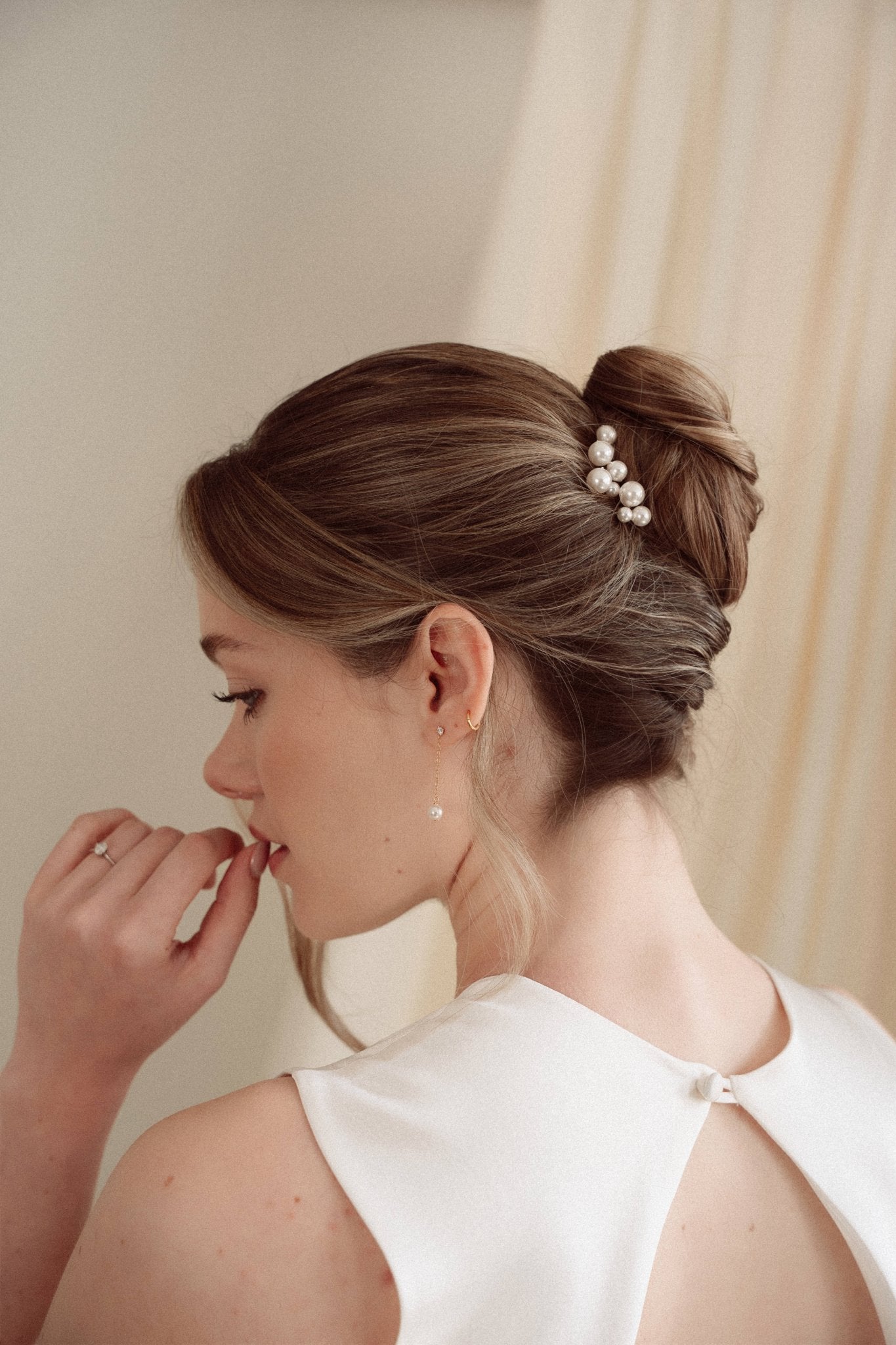 Bride wears pearl cluster hair pins and crystal and perl delicate drop earrings  with a silk gown and soft romantic chignon updo