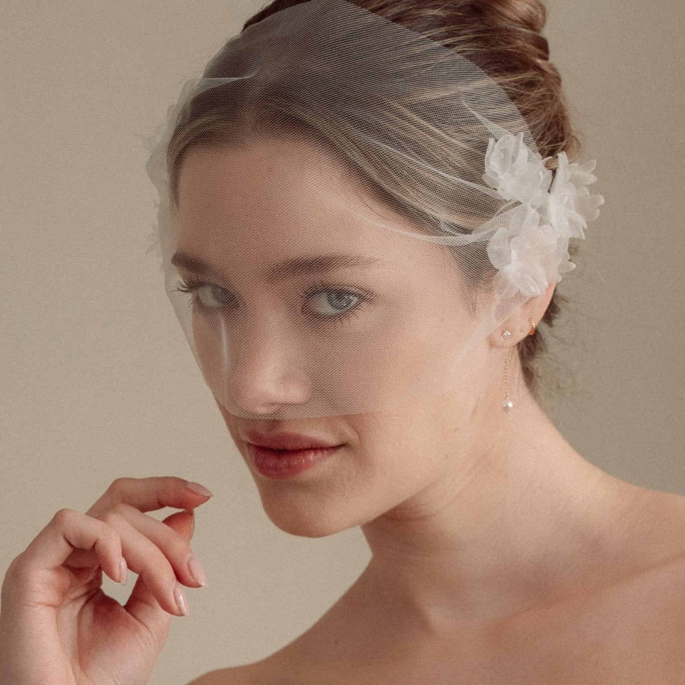 Bride wears an ivory tulle veil with face-framing silk flowers with coordinating silk flower and pearl long drop earrings