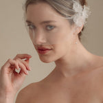Bride wears an ivory tulle veil with face-framing silk flowers with coordinating silk flower and pearl long drop earrings