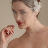 Bride wears an ivory tulle veil with face-framing silk flowers with coordinating silk flower and pearl long drop earrings