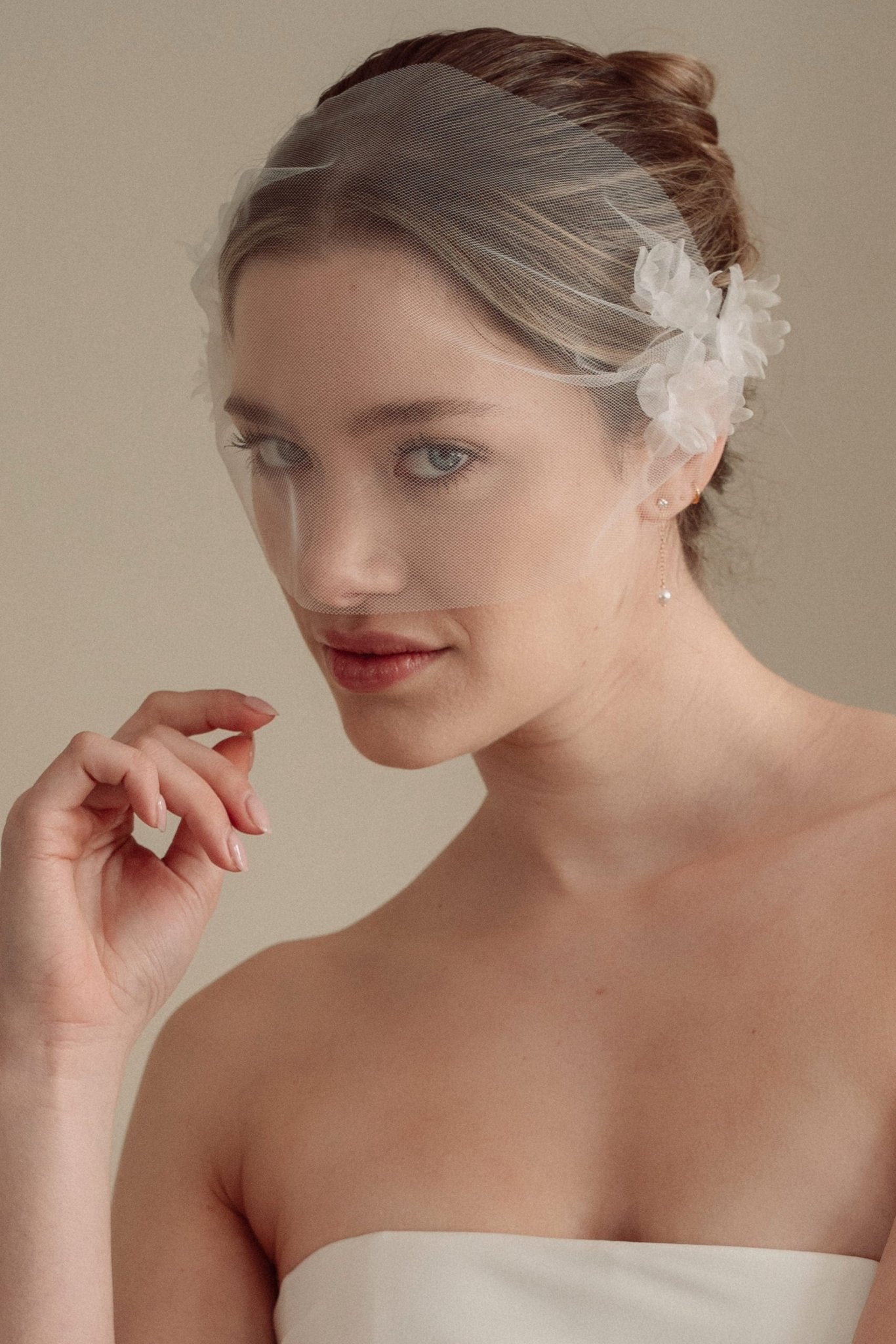 Bride wears an ivory tulle veil with face-framing silk flowers with coordinating silk flower and pearl long drop earrings