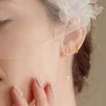 Bride wears an ivory tulle veil with face-framing silk flowers with coordinating silk flower and pearl long drop earrings