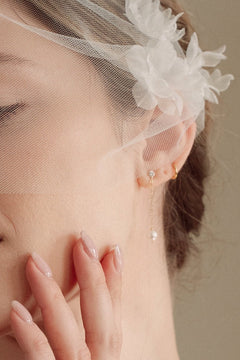 Bride wears an ivory tulle veil with face-framing silk flowers with coordinating silk flower and pearl long drop earrings