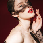 Woman in a black lace dress against a red background wears a black mask style micro veil with a lace edging
