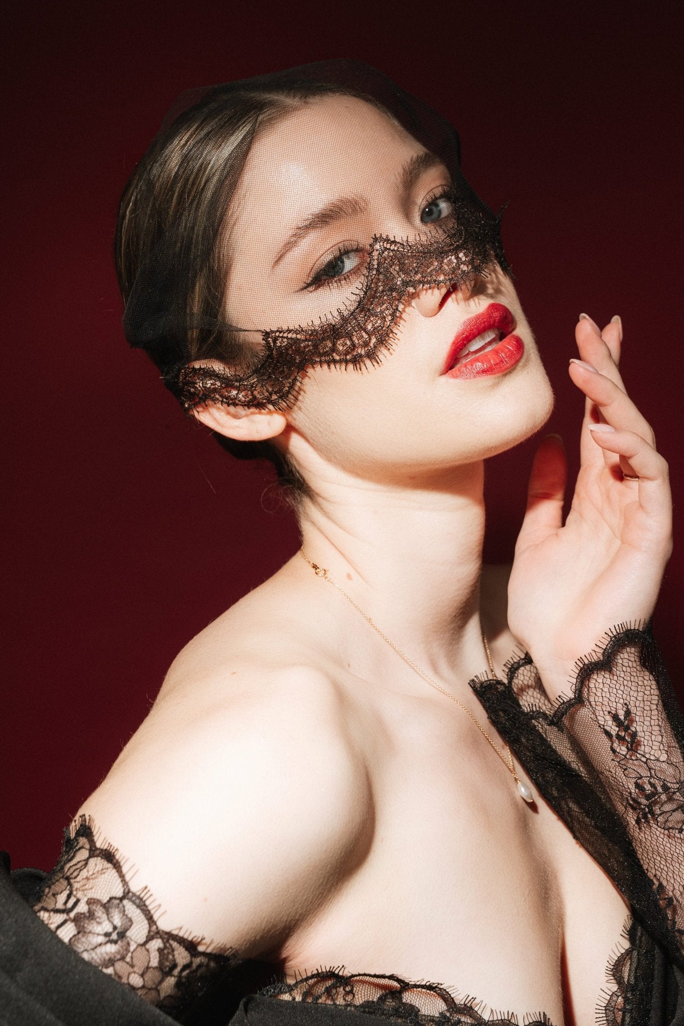 Woman in a black lace dress against a red background wears a black mask style micro veil with a lace edging