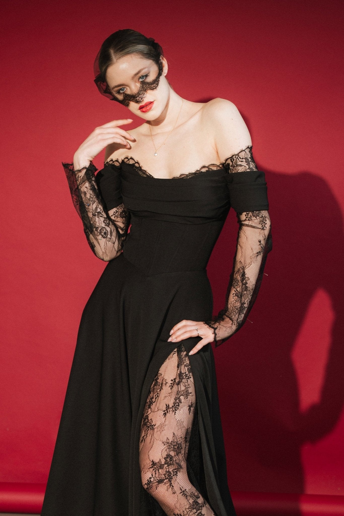 Woman in a black lace dress against a red background wears a black mask style micro veil with a lace edging