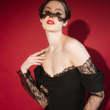 Woman in a black lace dress against a red background wears a black mask style micro veil with a lace edging