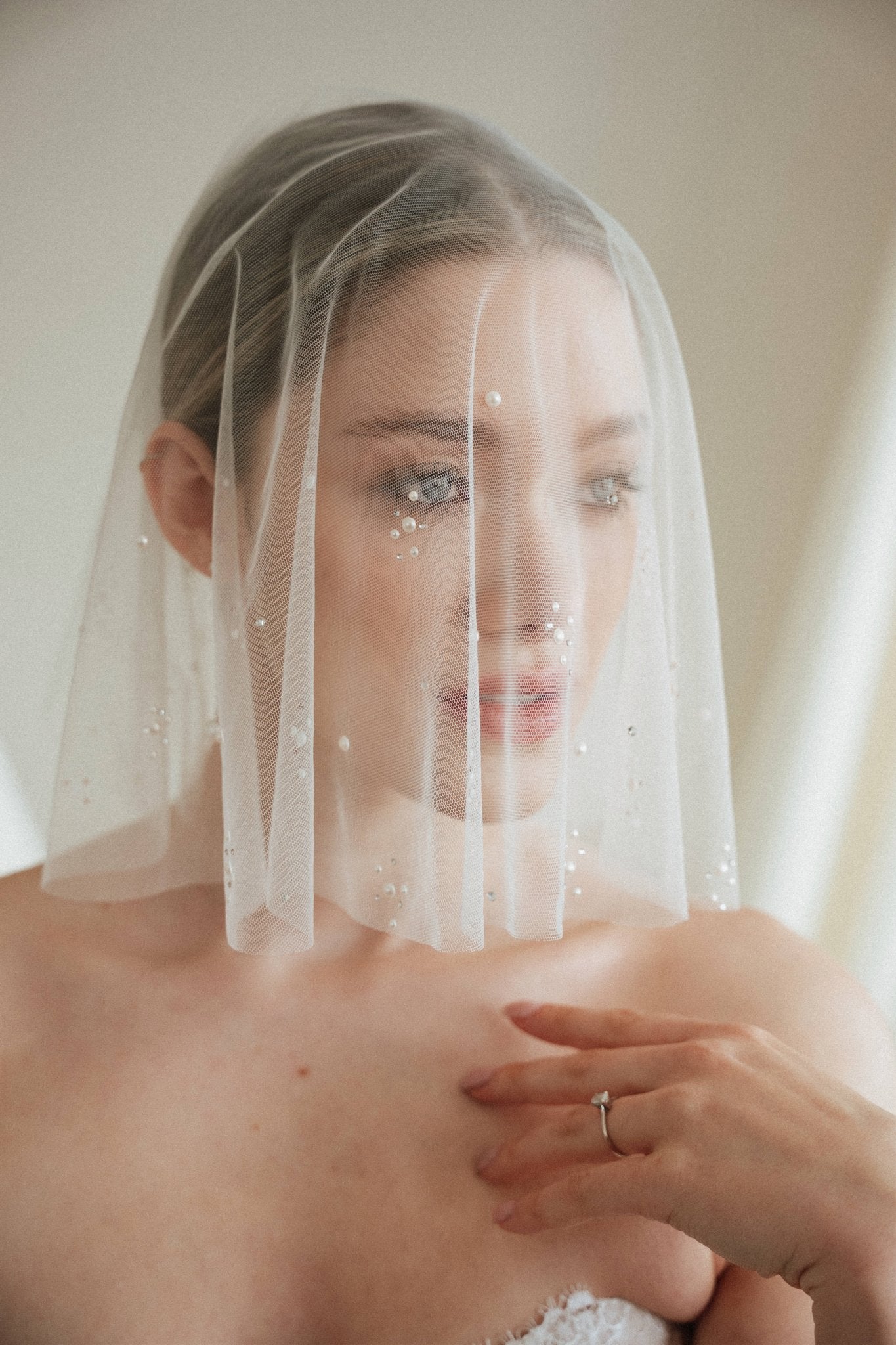 Bride wears a sheer tulle drop micro veil with pearl and crystal embellishments 