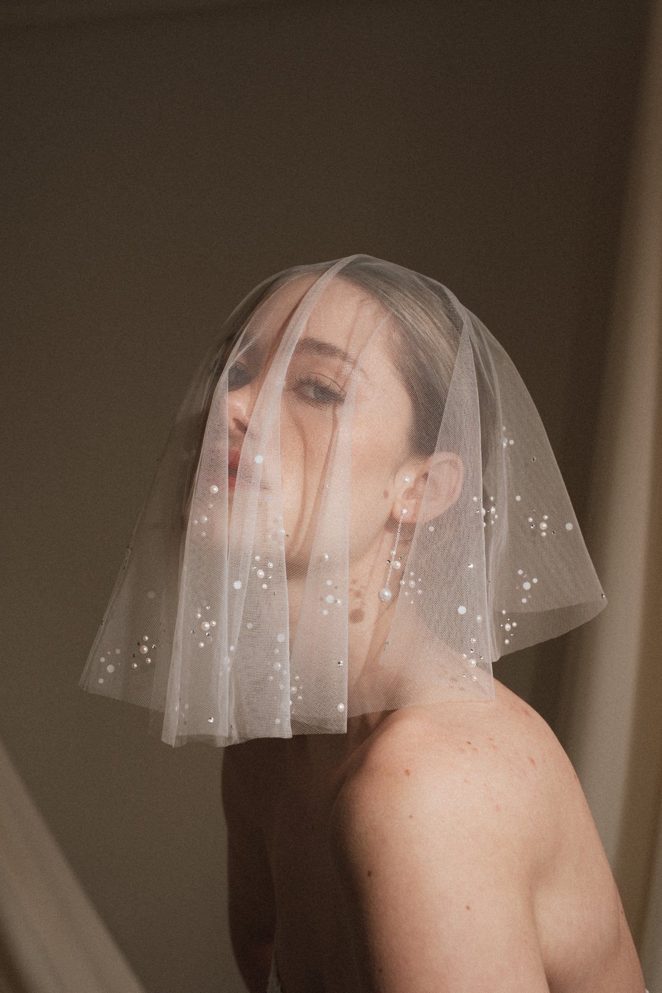 Bride wears a sheer tulle drop micro veil with pearl and crystal embellishments 