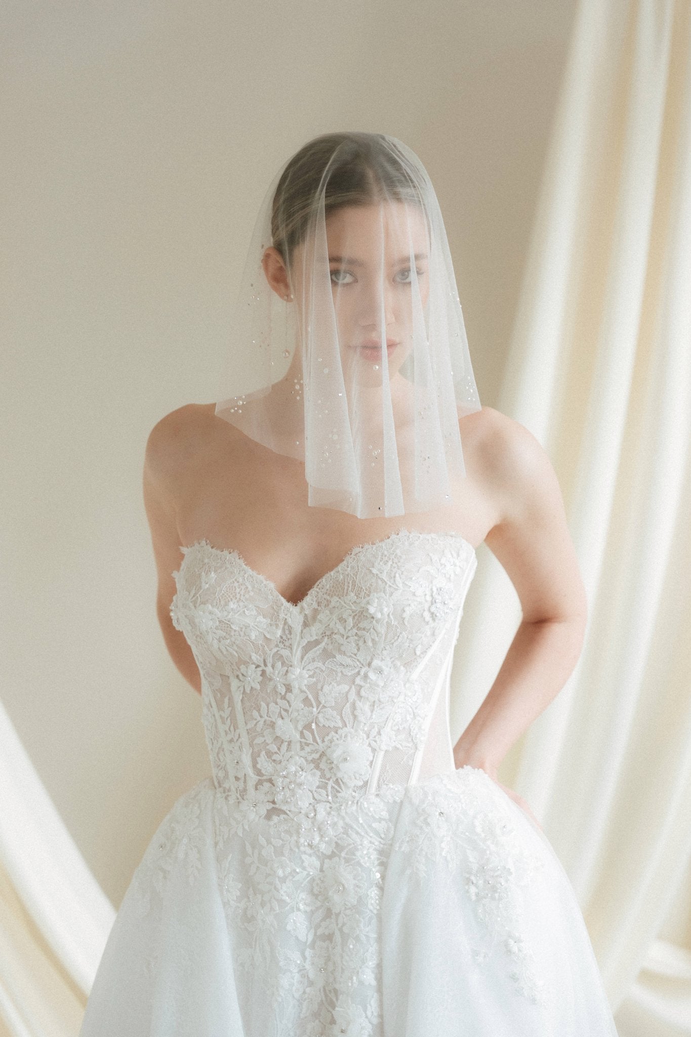 Bride wears a sheer tulle drop micro veil with pearl and crystal embellishments 