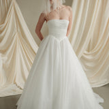 Woman wearing a white wedding dress with a bow-embellished veil against a neutral background
