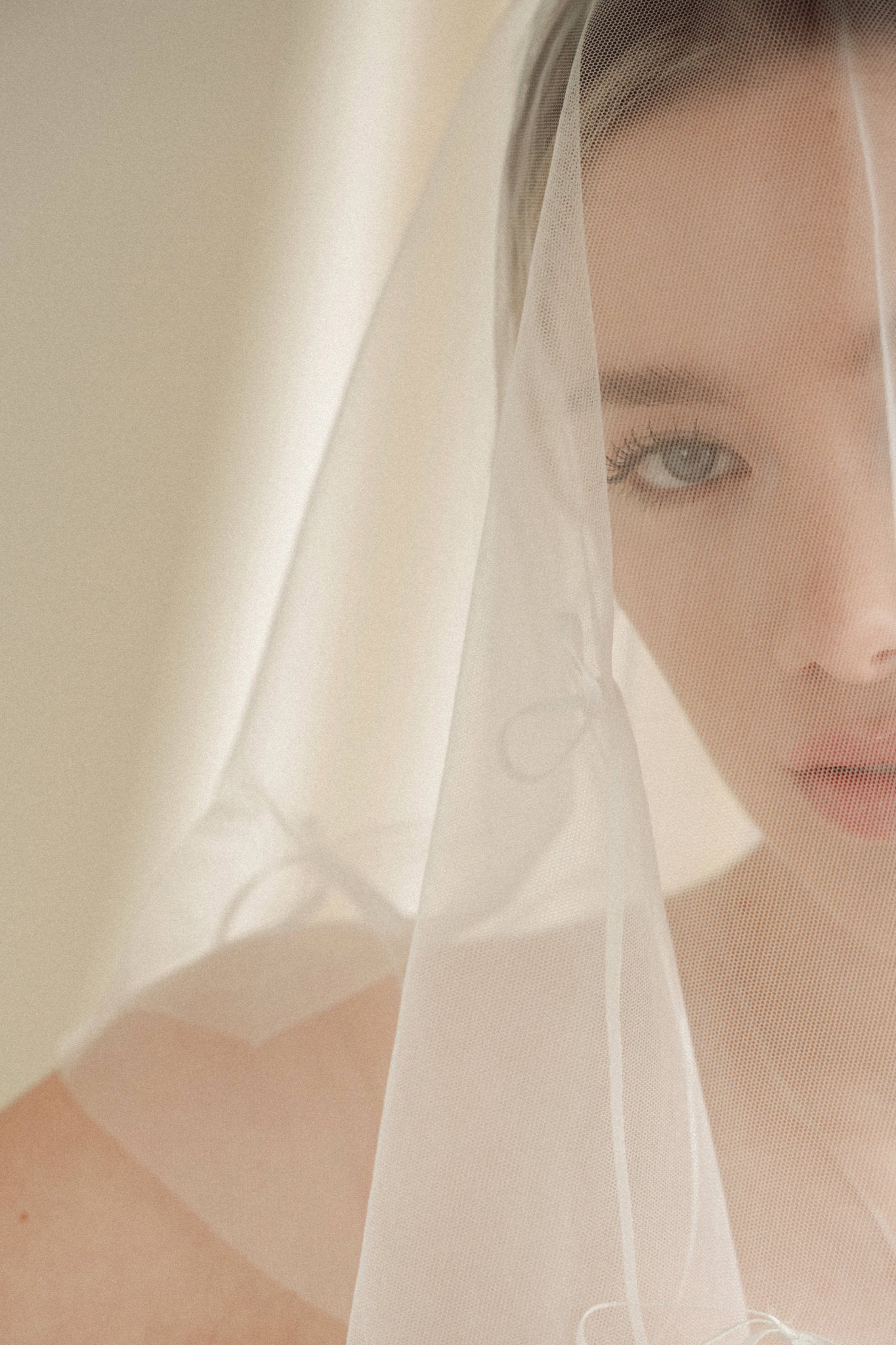 Woman wearing a white wedding dress with a bow-embellished veil against a neutral background