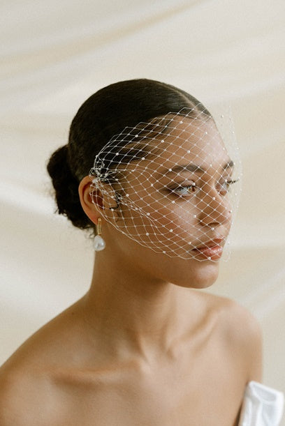 Brid wearing a pearl birdcage veil with a plain background