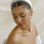 Merry Widow Graduated Crystal Birdcage Veil worn by a black bride with natural hair in a low bun with optional ivory satin padded headband and statement silver and pearl oblong hoop earrings