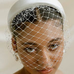 Merry Widow Graduated Crystal Birdcage Veil worn by a black bride with natural hair in a low bun with optional ivory satin padded headband and statement silver and pearl oblong hoop earrings