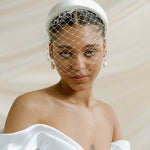 Merry Widow Graduated Crystal Birdcage Veil worn by a black bride with natural hair in a low bun with optional ivory satin padded headband and statement silver and pearl oblong hoop earrings
