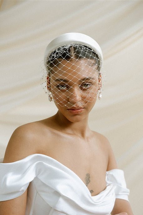 Merry Widow Graduated Crystal Birdcage Veil worn by a black bride with natural hair in a low bun with optional ivory satin padded headband and statement silver and pearl oblong hoop earrings