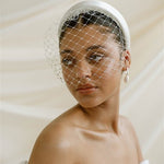 Merry Widow Graduated Crystal Birdcage Veil worn by a black bride with natural hair in a low bun with optional ivory satin padded headband and statement silver and pearl oblong hoop earrings