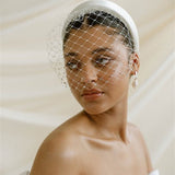 Merry Widow Graduated Crystal Birdcage Veil worn by a black bride with natural hair in a low bun with optional ivory satin padded headband and statement silver and pearl oblong hoop earrings