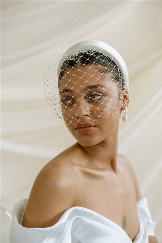 Merry Widow Graduated Crystal Birdcage Veil worn by a black bride with natural hair in a low bun with optional ivory satin padded headband and statement silver and pearl oblong hoop earrings