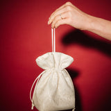 Hand holding a small ivory lace and satin drawstring bag against a red background