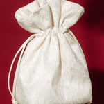Hand holding a small ivory lace and satin drawstring bag against a red background