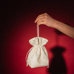 Hand holding a small ivory lace and satin drawstring bag against a red background