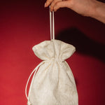 Hand holding a small ivory lace and satin drawstring bag against a red background