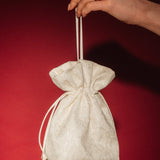 Hand holding a small ivory lace and satin drawstring bag against a red background