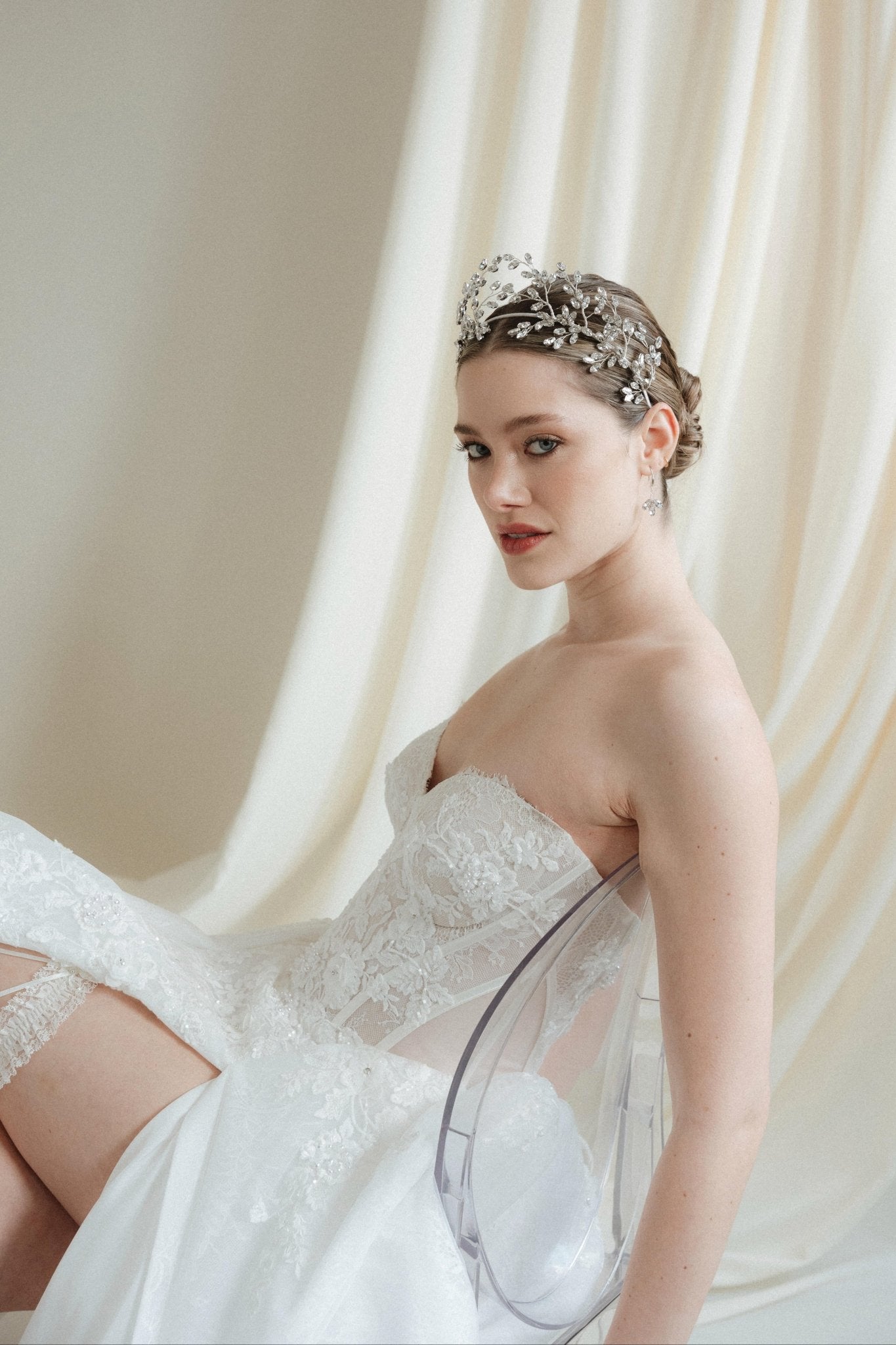 bride in a white wedding dress reclines in a crown against an ivory draped background